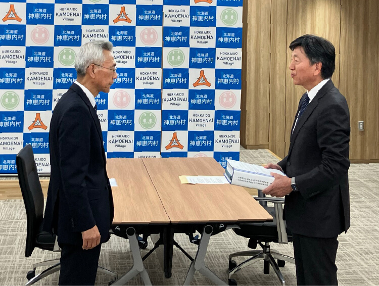 青塚副村長へ報告書を手渡す山口理事長（右）（神恵内村役場にて）